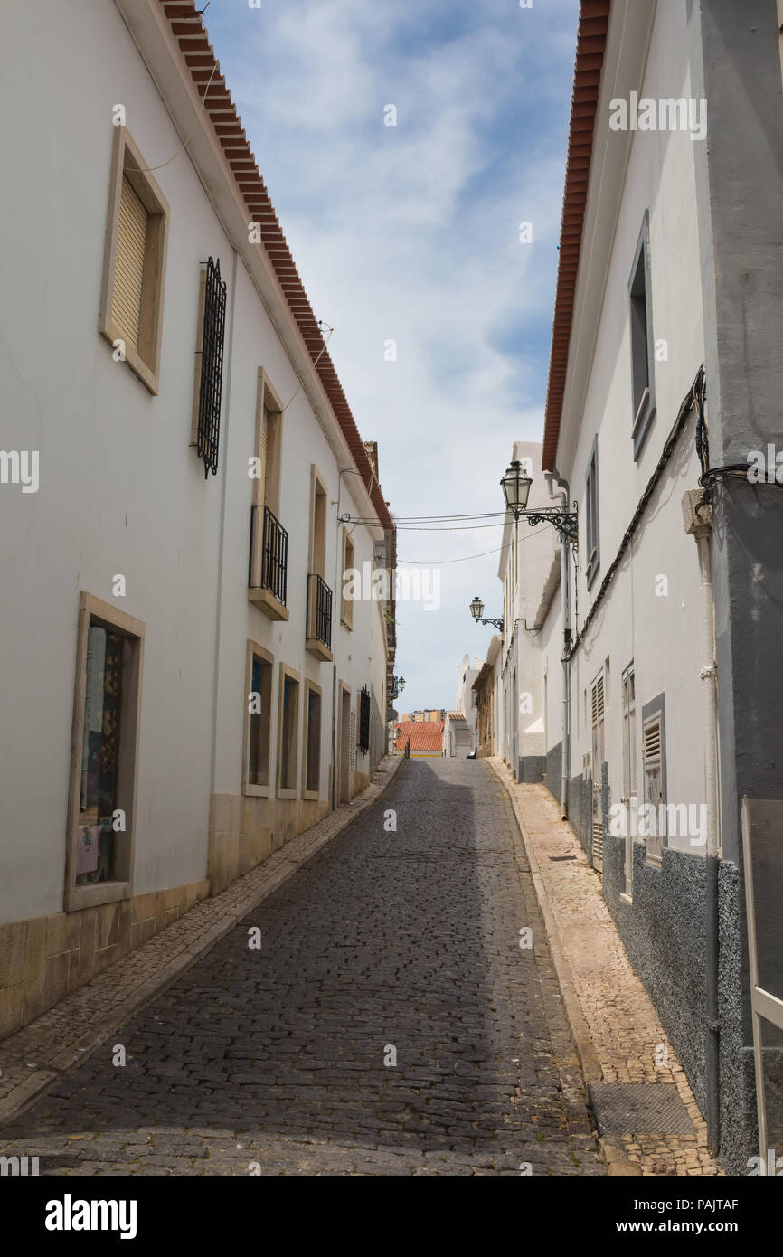 Schmale Straße den Hügel hinauf, von weißen Häusern und gepflasterten durch Kopfsteinpflaster. Traditionelle Laternen. Zeile der Dachziegel. Bewölkter Himmel. Lagos, Algarve, P Stockfoto