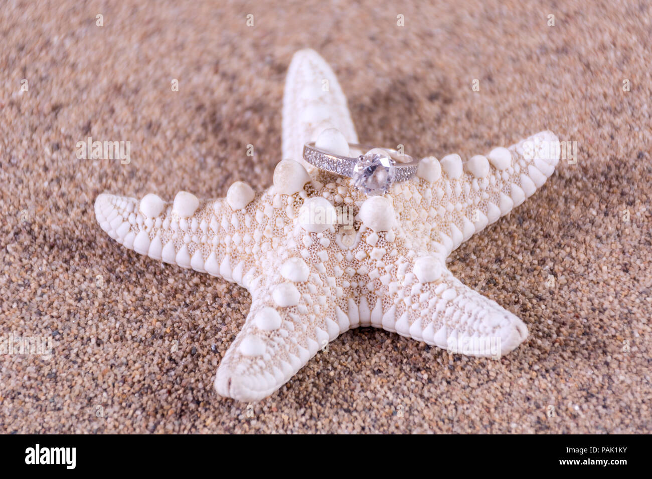 Diamant Verlobung Hochzeit Ring am Seestern auf sandigen Strand, verschwommen und weichen Sand. Schmuck Konzept. Close Up, selektiver Fokus Stockfoto
