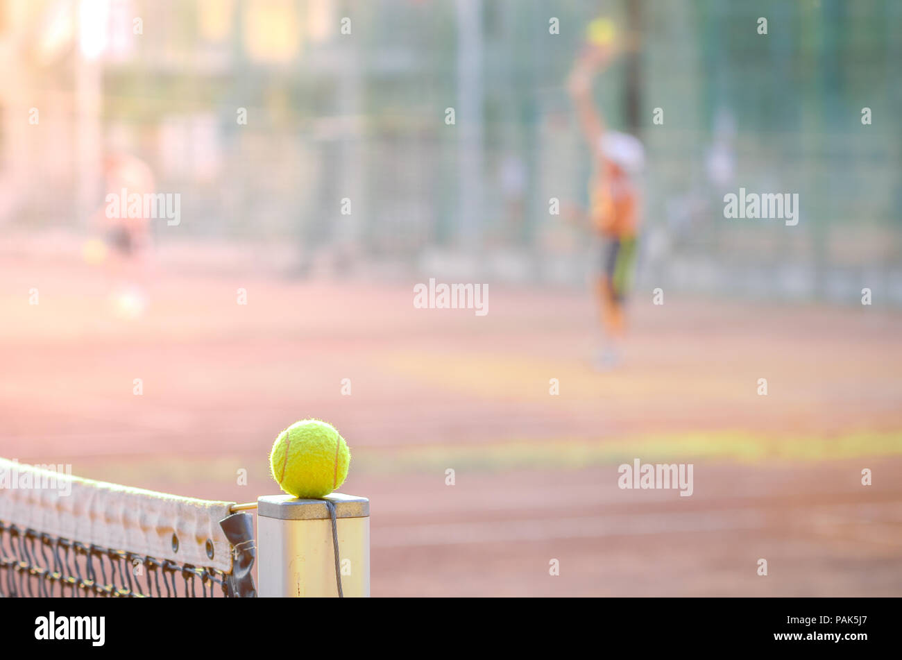 Tennis Spieler auf einem Sandplatz mit einem gelben Ball im Fokus auf einem Net post was auf eine harte Tennis Spiel mit Soft Filter Effekte angewendet Stockfoto