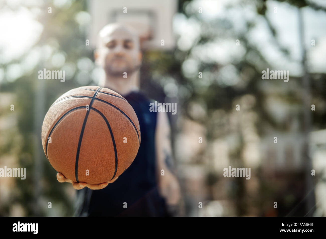 In der Nähe des Kahlen attraktiver Mann mit Korb Ball. Kugel in den Mittelpunkt und Vordergrund. Mann, Basketballkorb und Brett sind auf Hintergrund und verschwommen. Stockfoto