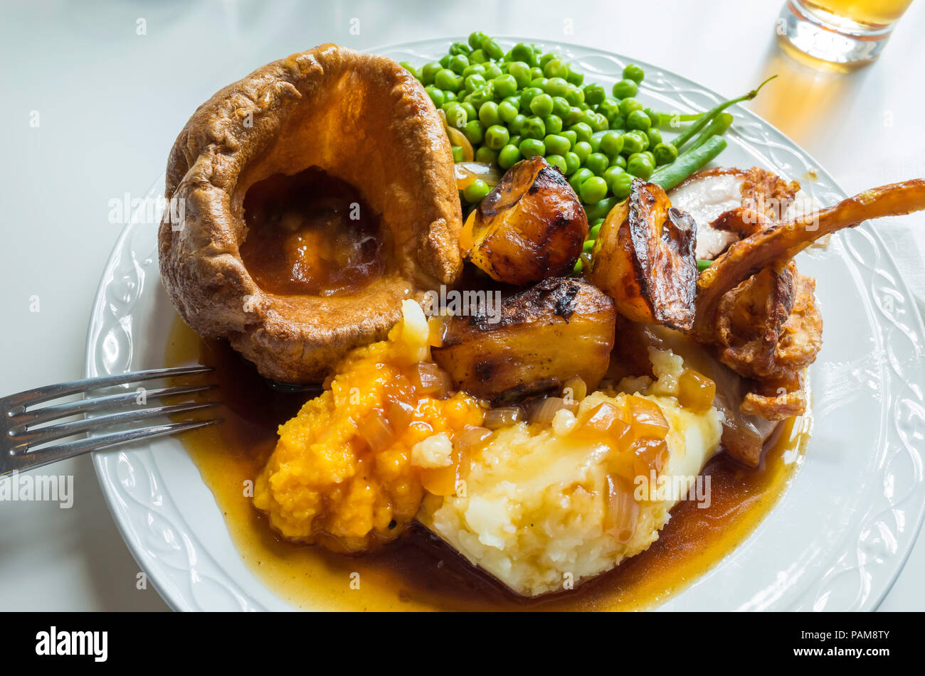 Traditionelle englische Mittagessen am Sonntag Schweinebraten mit Yorkshire Pudding, Kartoffelpüree und Röstkartoffeln Schwede Erbsen Grüne Bohnen und Soße Stockfoto