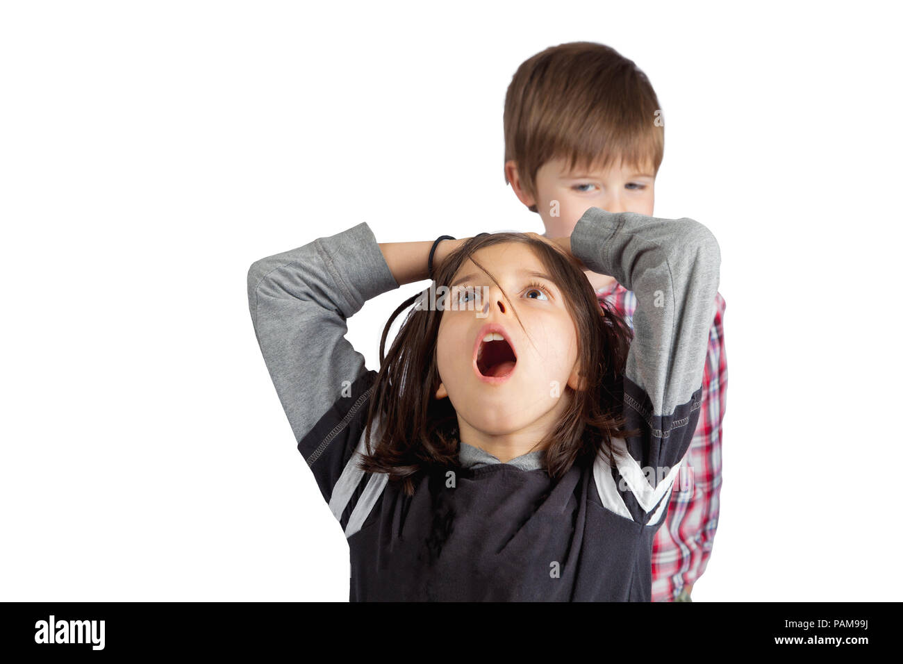 Einen kleinen Bruder zieht das Haar von seiner älteren Schwester. Er sieht schlau und gerissen. Sie packt ihren Kopf mit einem offenen Mund Blick von Schock und Schmerz. Stockfoto