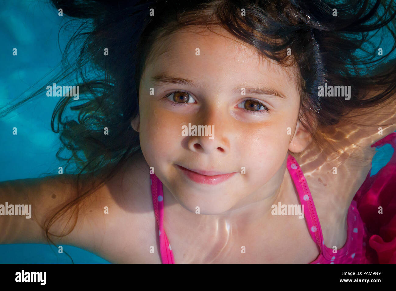 Ein Junges Madchen Mit Grossen Braunen Augen Schwimmt In Einem Blauen Pool Mit Ihrem Haar Fliesst Um Ihr Gesicht Auf Der Flache Der Wasser Sie Sucht Auf Dem Nocken Stockfotografie Alamy