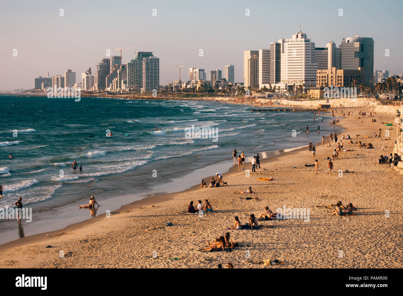 Der Strand ist gesprenkelt mit Sonnenanbeter, während die Skyline von Tel Aviv auf während einem Sommer Sonnenuntergang in Alma Strand, Tel Aviv-Jaffa, Israel sieht Stockfoto