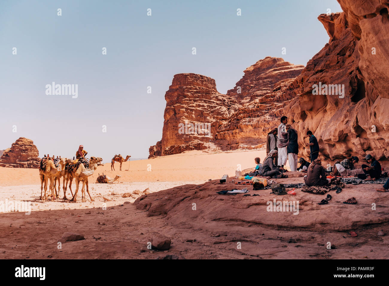 Bedouin Zuflucht im Schatten und etwas zu Essen vorbereiten, während ihre Kamele in der prallen Sonne der Wüste im Wadi Rum, Jordanien geparkt, Stockfoto