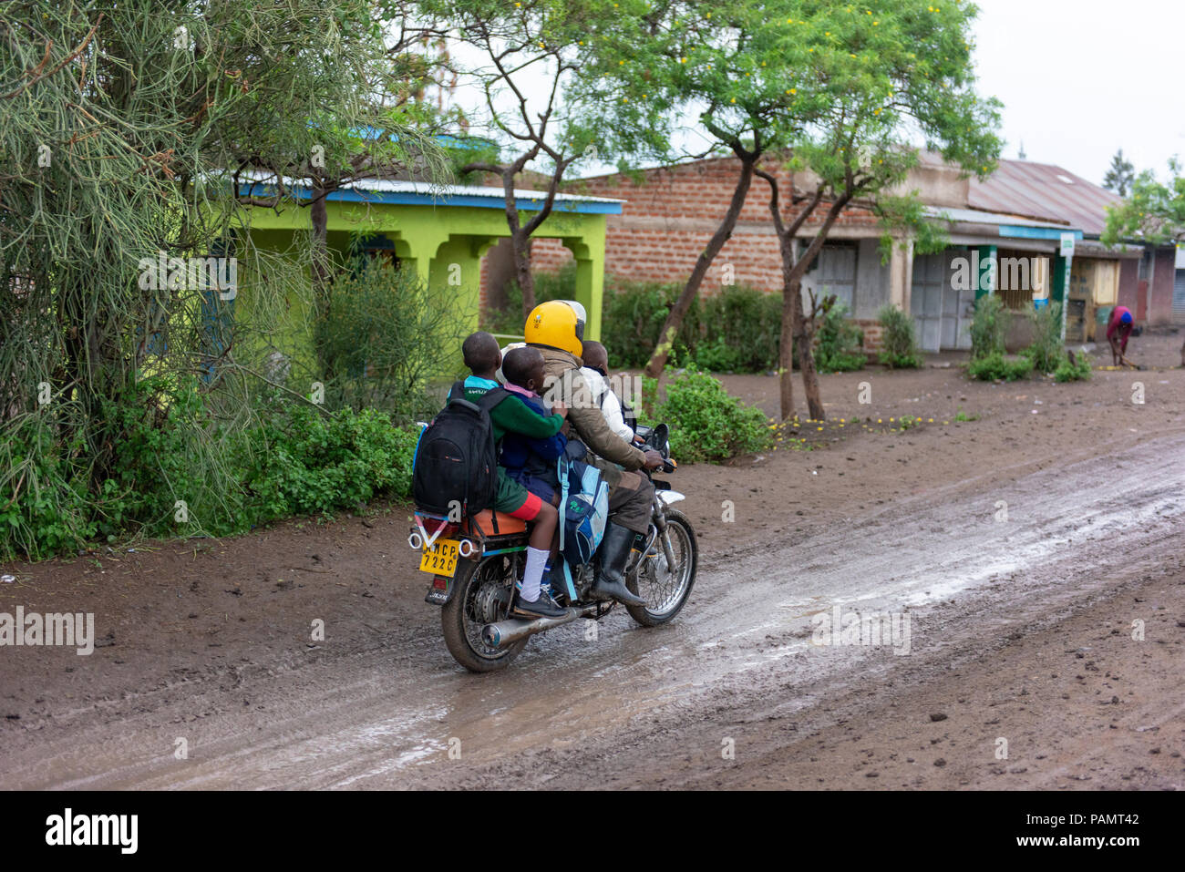 Ein Mann nimmt seine Kinder auf einem Motorrad auf schlechten Straßen zur Schule nach dem Regen. Stockfoto