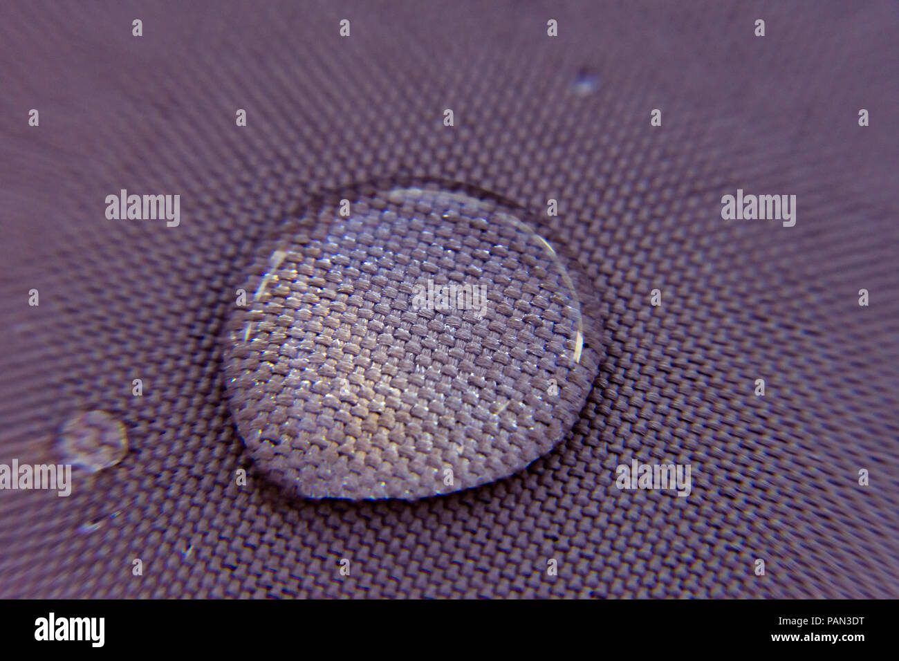 Wassertropfen auf eine wasserfeste Oberfläche mit den Details der Stoff durch den transparenten Tropfen. Stockfoto
