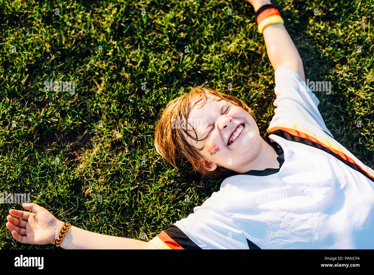 Junge im deutschen Fussball shirt liegen auf Gras, laughimg Stockfoto
