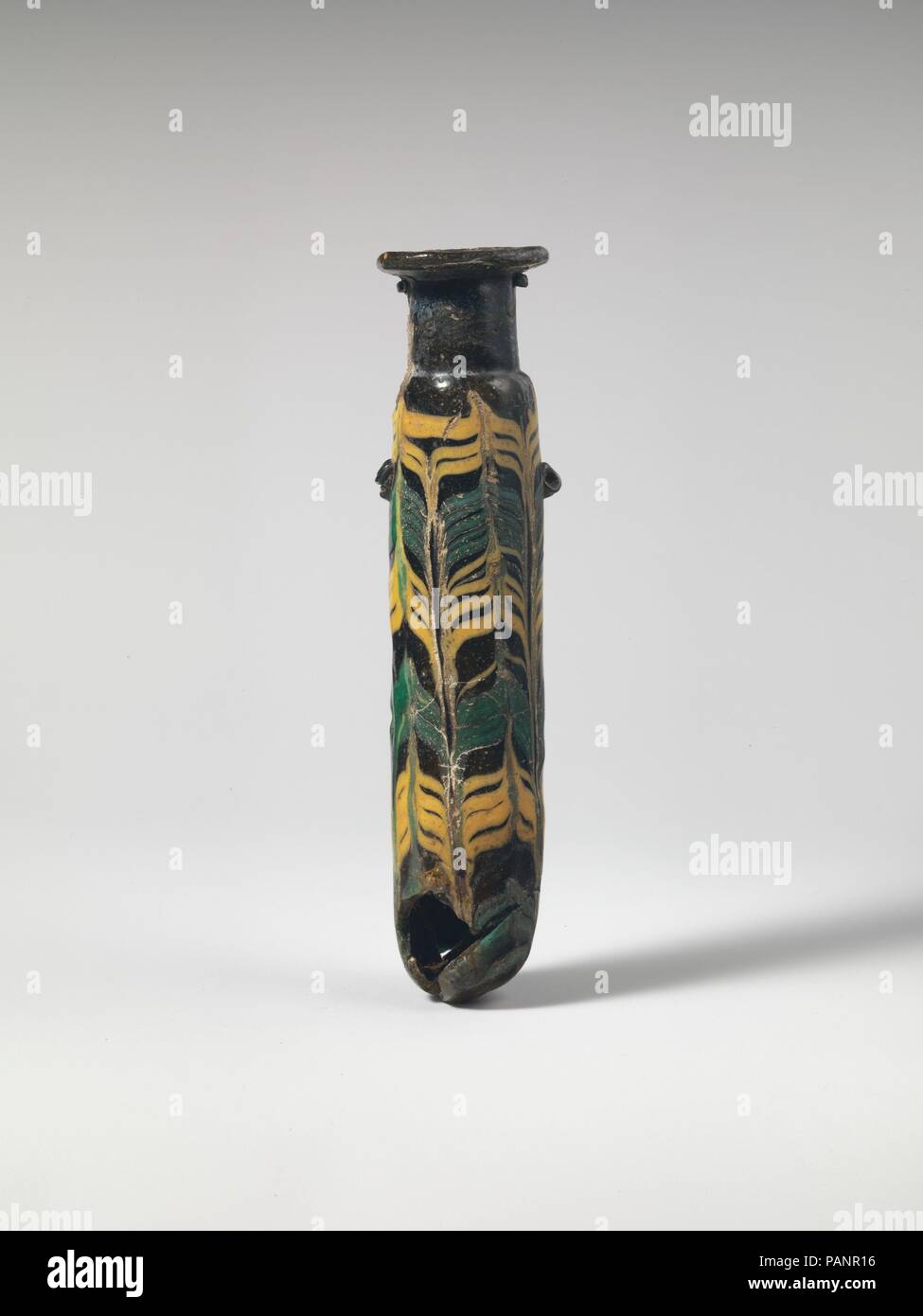 Glas alabastron (Parfüm Flasche). Kultur: Griechisch, östlichen Mittelmeer. Abmessungen: H.: 4 7/8 in. (12,4 cm). Datum: Ende 4./Anfang 3.Jh. v. Chr.. Transluzente blass gelblich grün mit dunkleren Blau Grün Streifen, mit Griffen in der gleichen Farbe; Wanderwege in Opak gelb, opak türkis blau. Horizontale rim-disk; hohe zylindrische, schrägen Hals; kleine schräge Schulter; Gerade-seitig zylindrische Körper, mit leicht nach oben Konus; konvexen Boden aber mit off-center Spitze; auf Körper, zwei Stift griffen, über trail Muster angewendet. eine werkzeuggestützte nach oben horizontal Gedankenstrich, der andere mit einem sidew Stockfoto