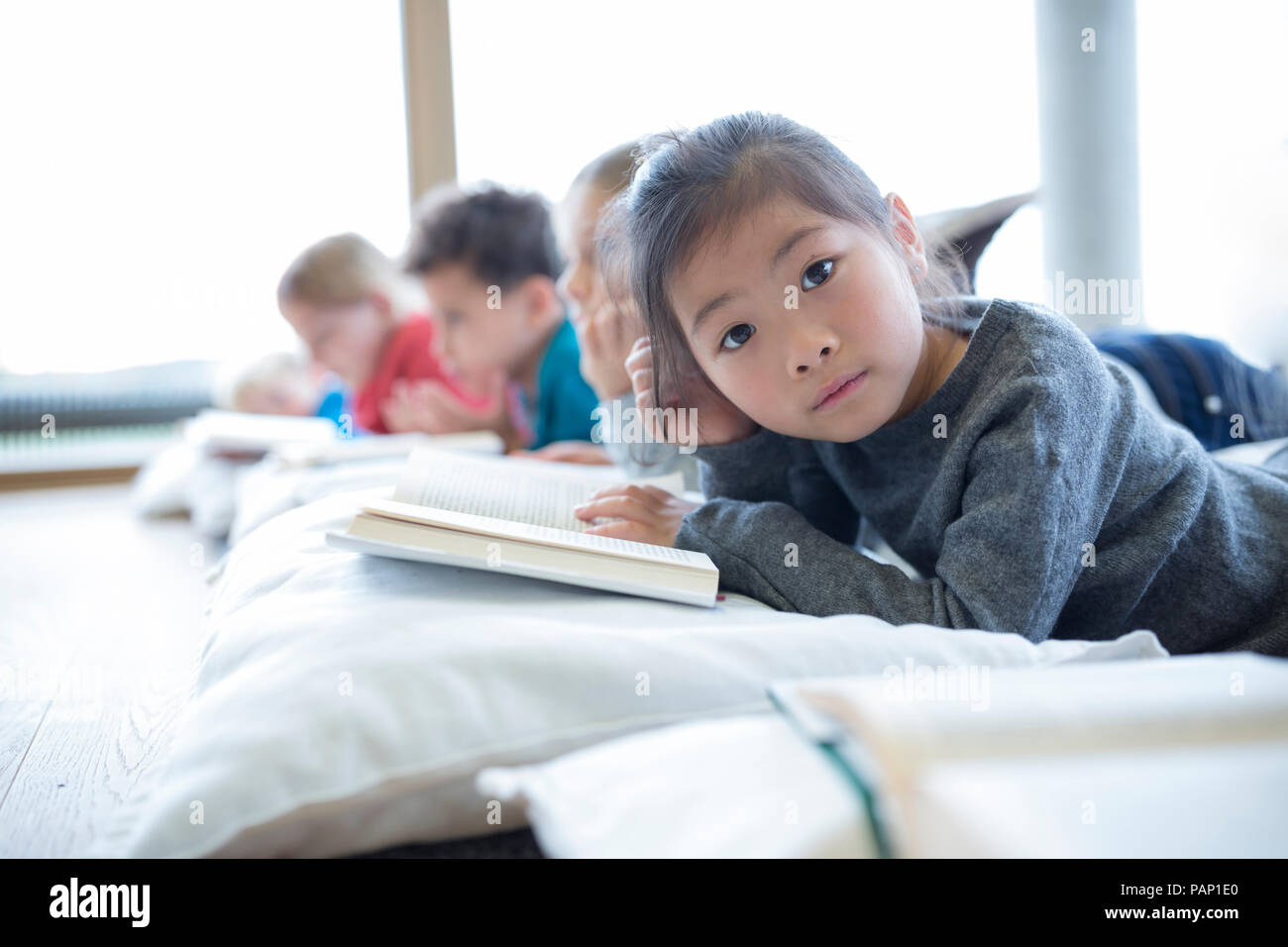 Portrait von Schulmädchen auf dem Boden liegend mit Mitschülern lesen Buch in der Schule pause Zimmer Stockfoto