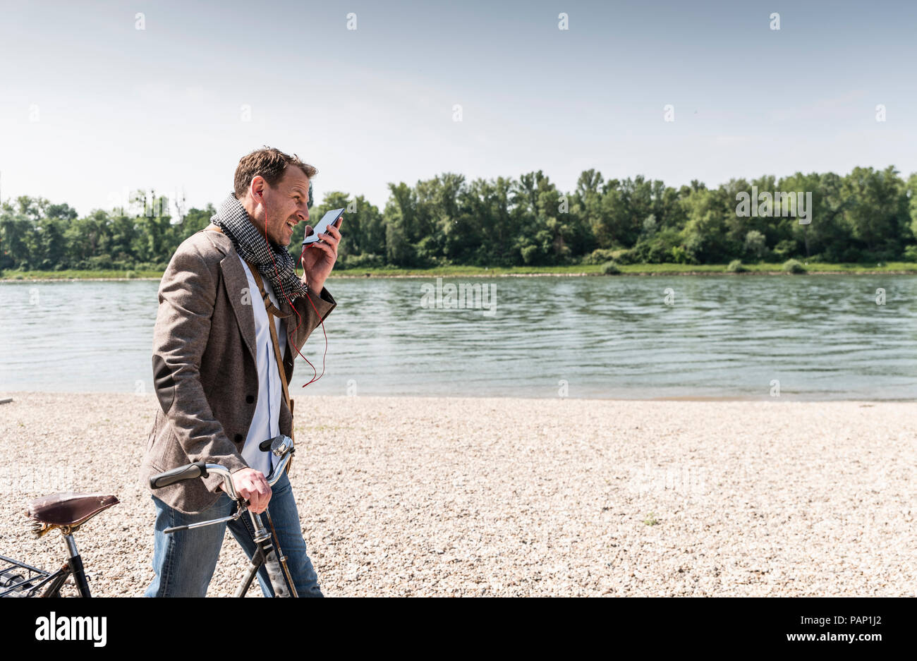 Reifer Mann mit Fahrrad mit an Rhein Ufer smartphone Stockfoto