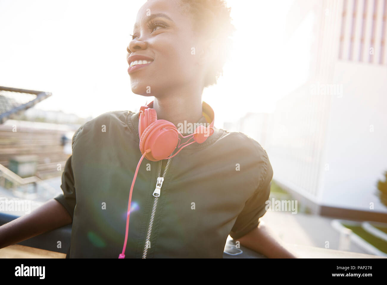 Lächelnde junge Frau mit Kopfhörern mit Hintergrundbeleuchtung Stockfoto