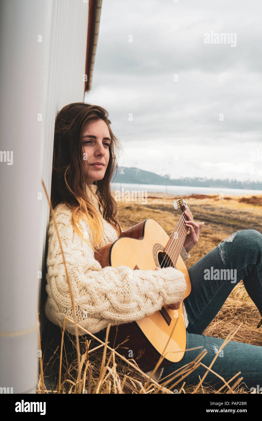 Island, Frau in ländlichen Landschaft Gitarre spielen Sitzen Stockfoto