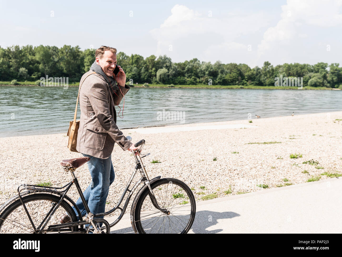 Reifer Mann mit Fahrrad mit an Rhein Ufer smartphone Stockfoto