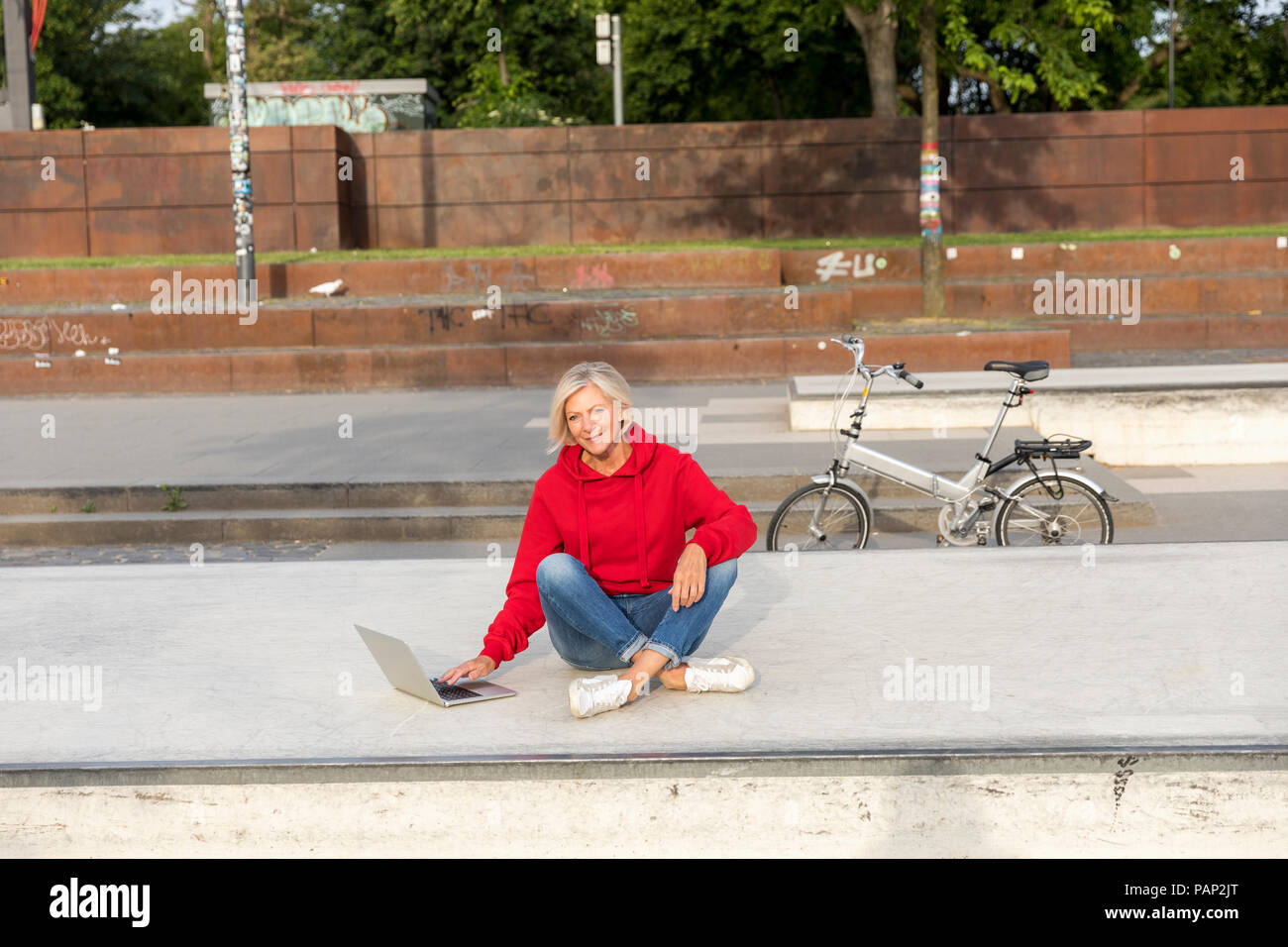 Ältere Frau in Rot hoodie mit Laptop im Freien Stockfoto