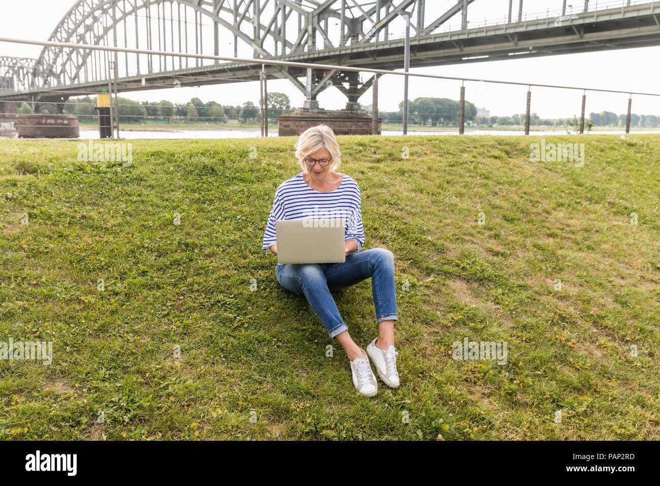 Ältere Frau sitzt auf einem Deich mit Laptop Stockfoto