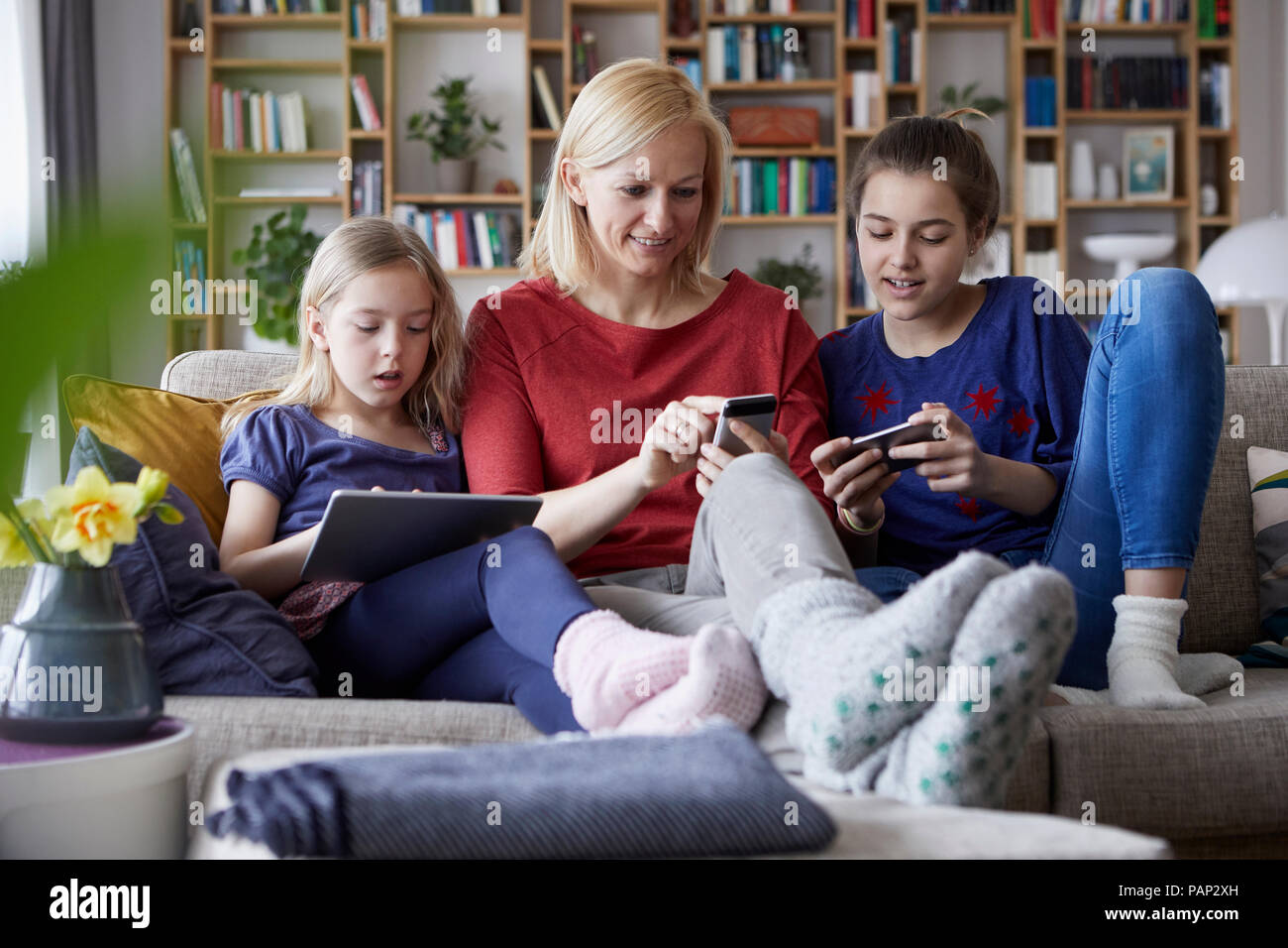 Mutter und ihre Töchter auf der Couch sitzen, Spaß mit digitalen Laptop und Spielen mit Smartphones Stockfoto