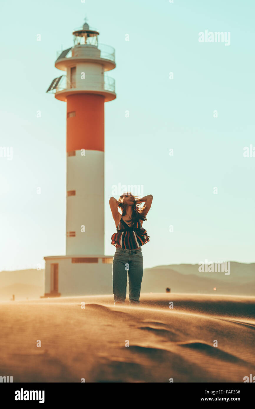 Junge Frau mit windswept Haare stehen in der Wüste Landschaft am Leuchtturm Stockfoto