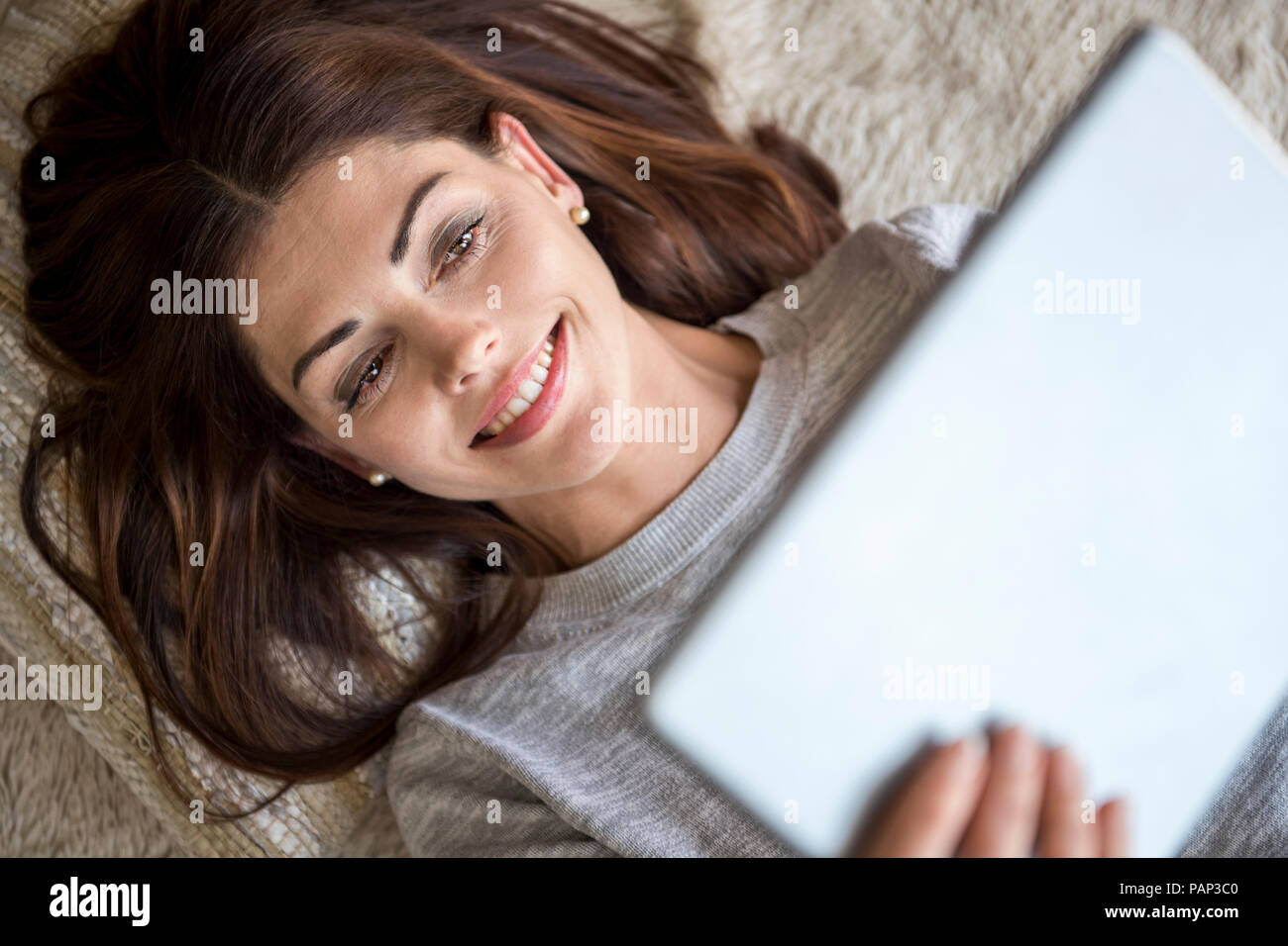 Lächelnde Frau liegend auf dem Teppich mit einem Tablet Stockfoto