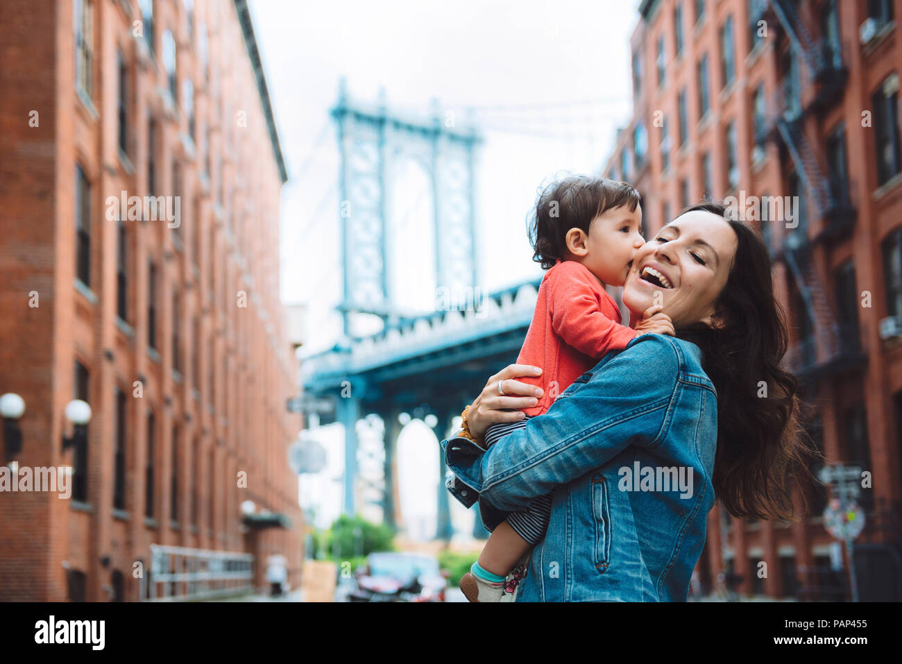 USA, New York, New York City, Baby küssen Mutter in Brooklyn mit Manhattan Bridge im Hintergrund Stockfoto