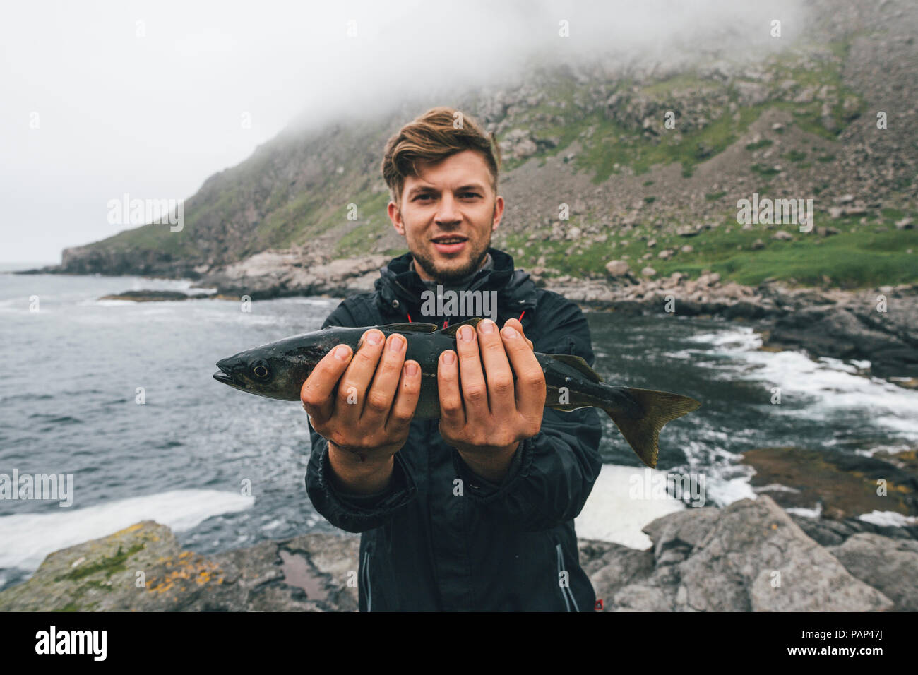 Norwegen, Lofoten, Moskenesoy, junger Mann mit frisch gefangenen Fisch bei Horseid Strand Stockfoto