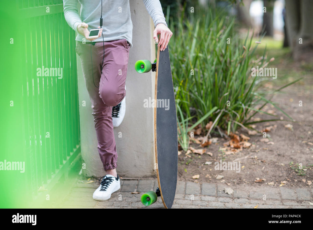 Close-up boy Holding Skateboard und mit Handy Stockfoto