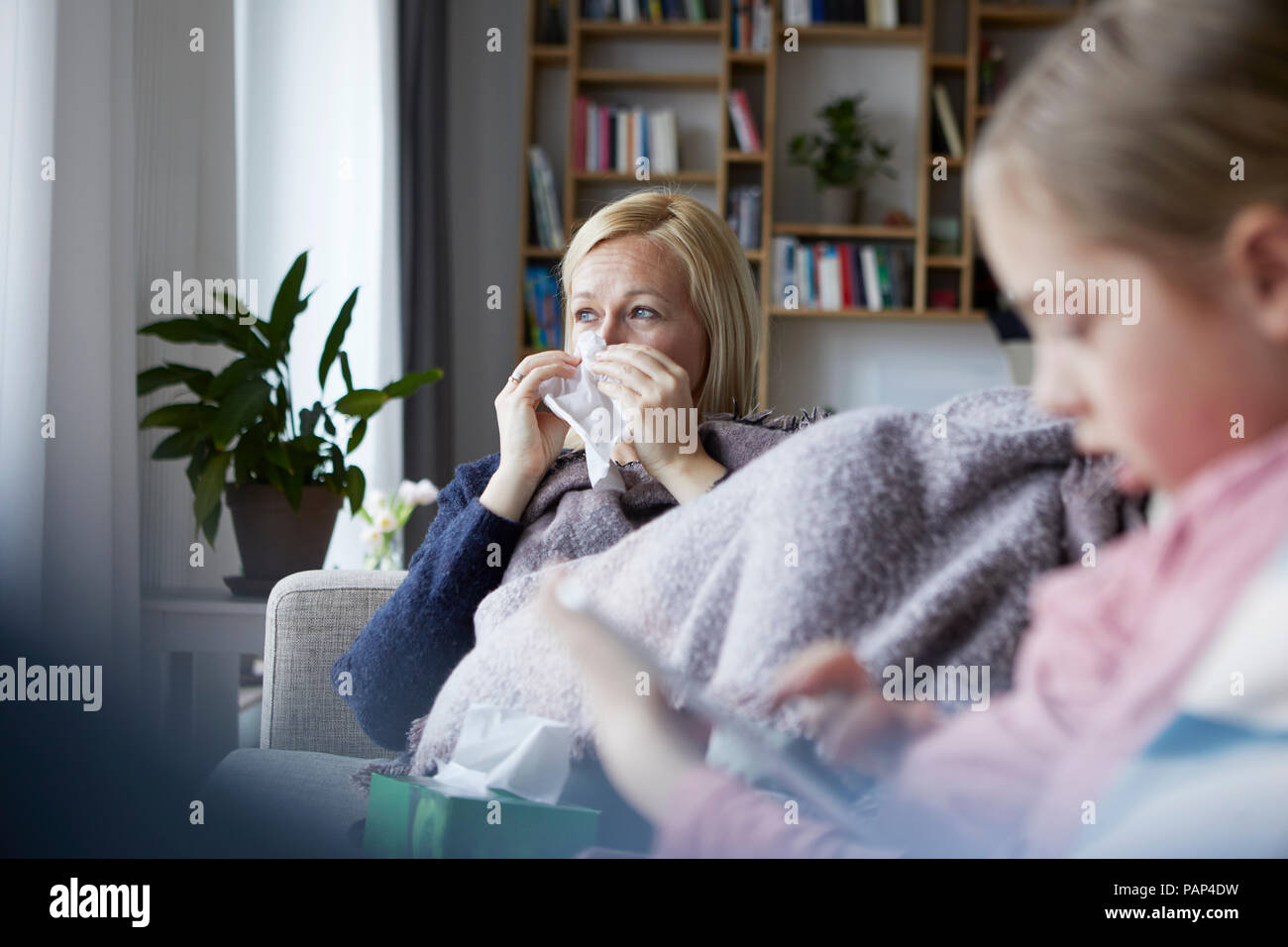 Mutter sitzt auf der Couch, mit einem kalten, Tochter spielen in den Vordergrund. Stockfoto