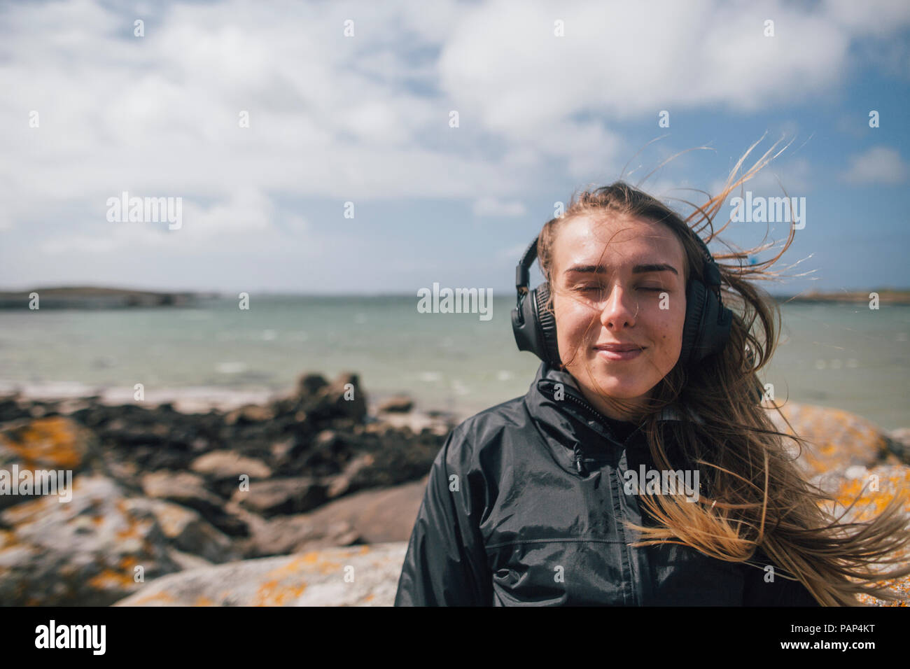 Frankreich, Bretagne, Landeda, lächelnden jungen Frau Kopfhörer tragen an der Küste Stockfoto