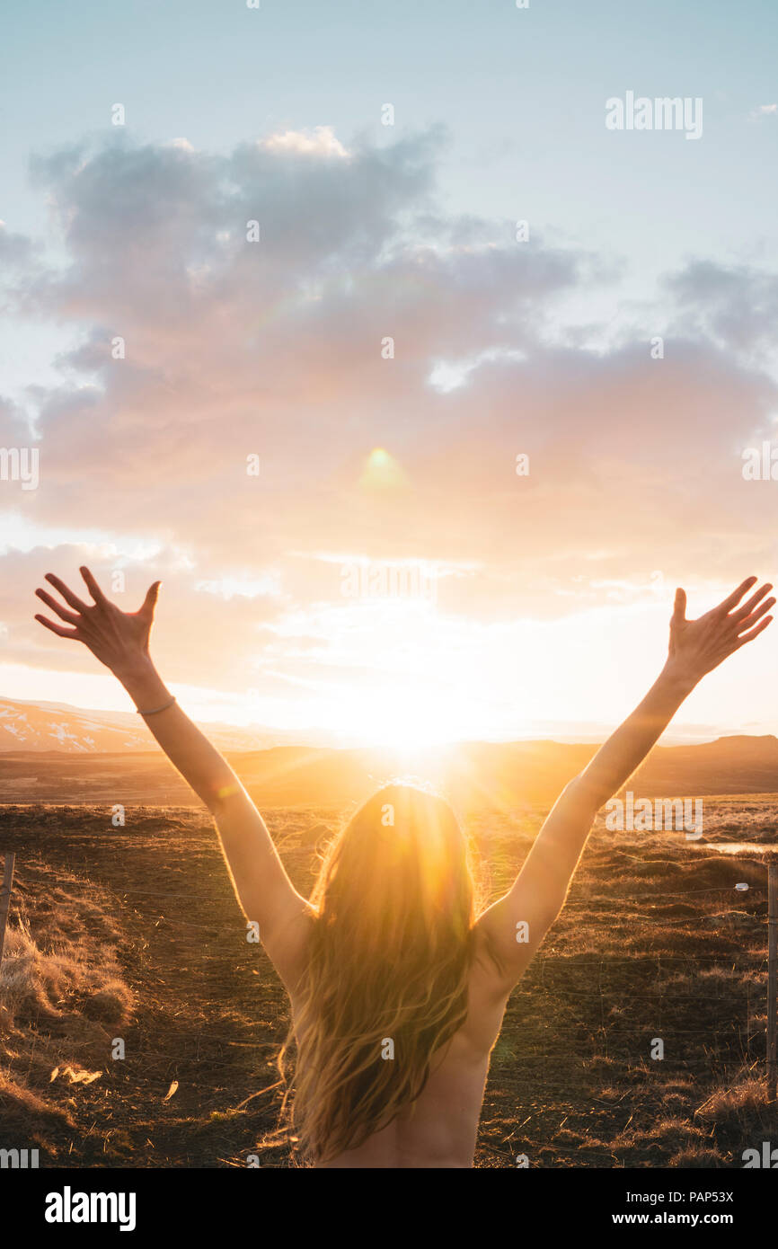 Island, junge Frau mit erhobenen Armen bei Sonnenuntergang Stockfoto