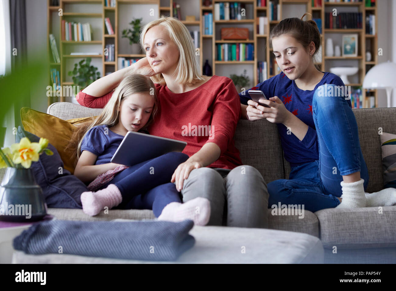 Traurige Mutter sitzt auf der Couch und ihre Töchter, spielen mit mobilen Geräten Stockfoto
