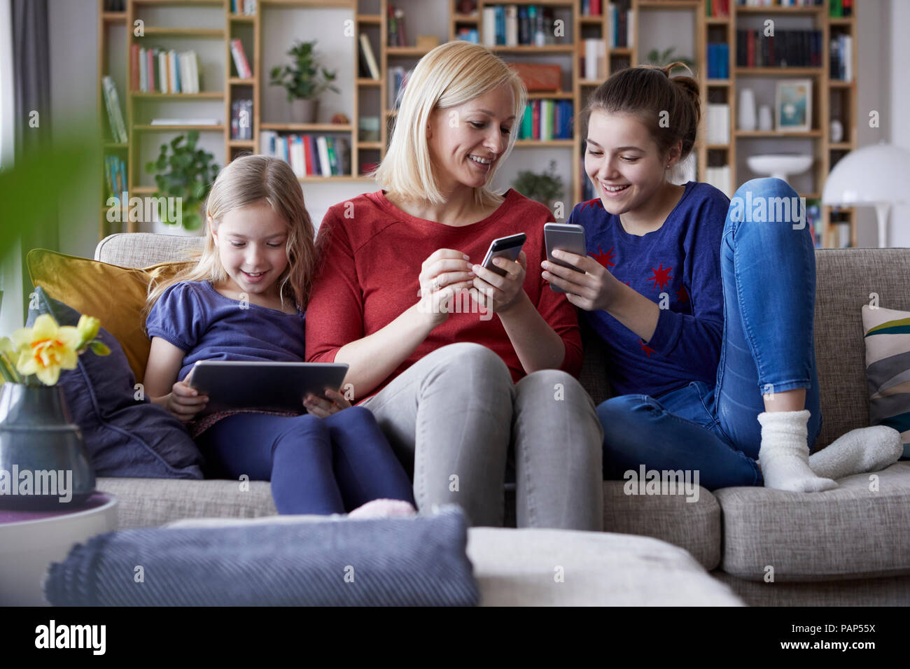 Mutter und ihre Töchter auf der Couch sitzen, Spaß mit digitalen Laptop und Spielen mit Smartphones Stockfoto