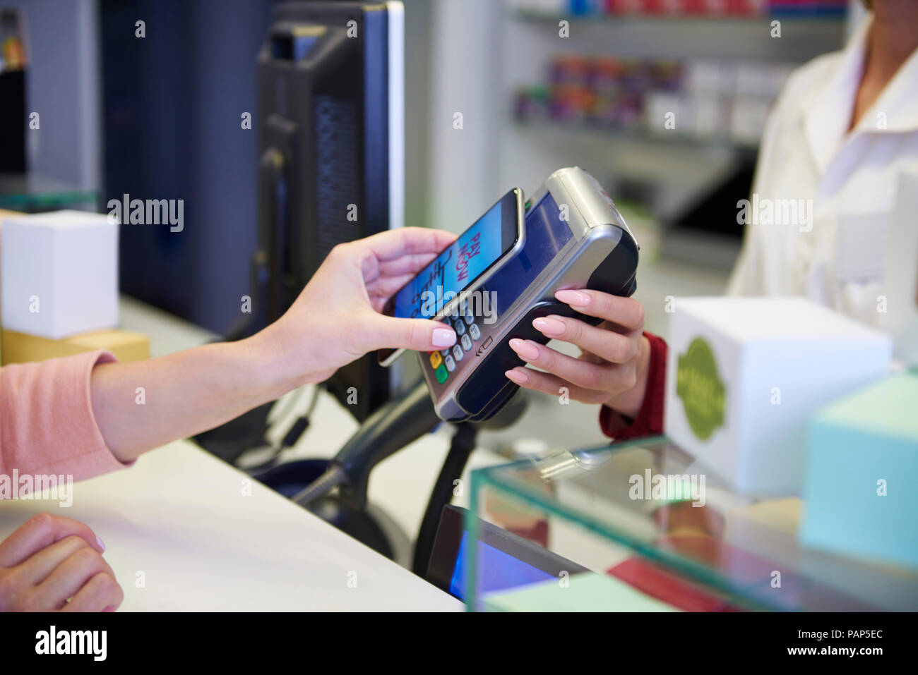 Kunden bezahlen bargeldlos mit Smartphones in der Apotheke Stockfoto