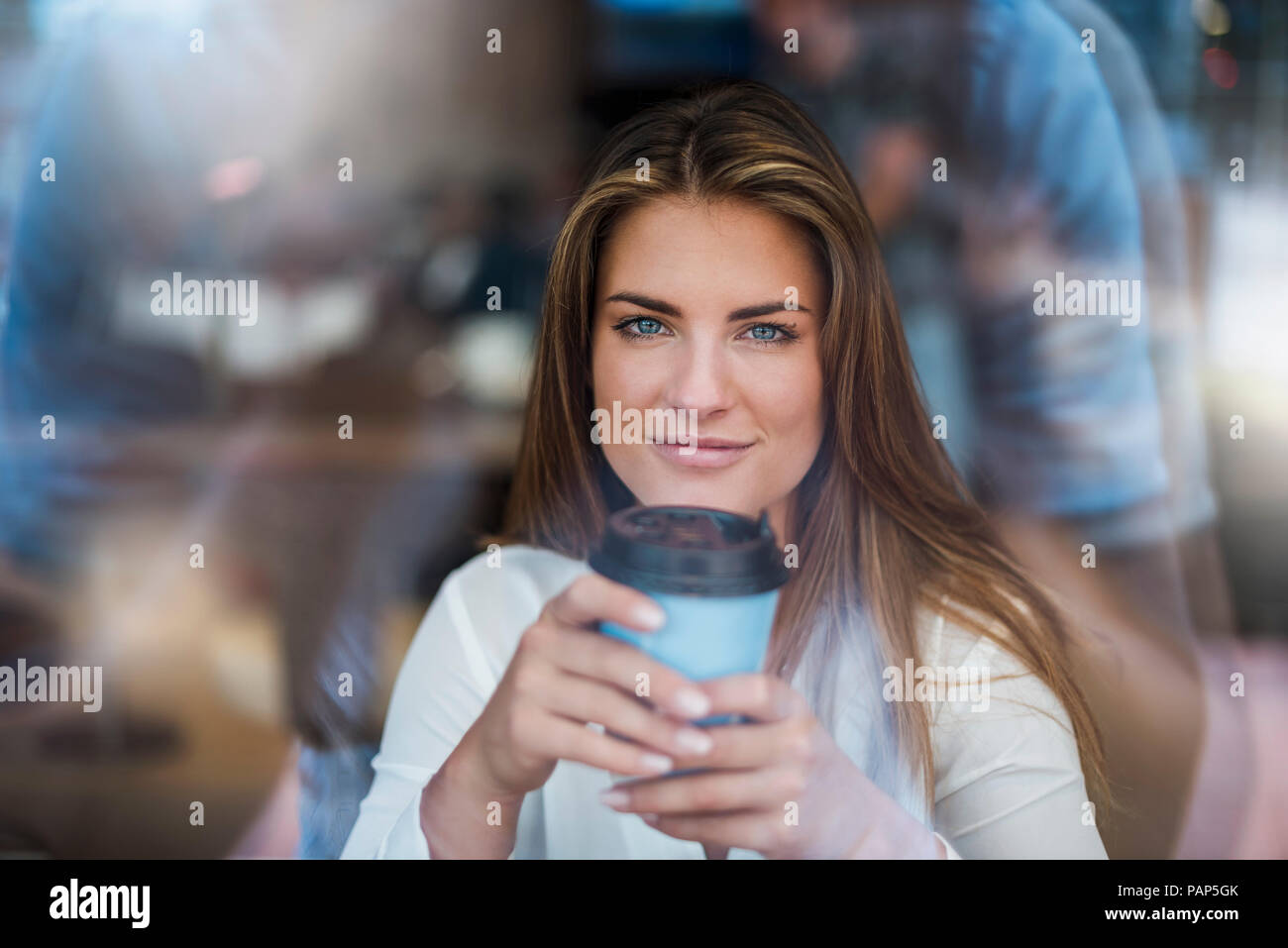 Portrait von lächelnden jungen Frau hinter Fensterglas mit Kaffee zum Mitnehmen Stockfoto