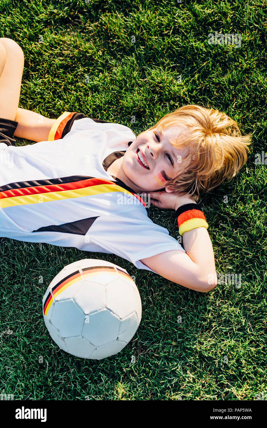 Junge im deutschen Fussball Shirt, lächelnd im Gras liegend Stockfoto