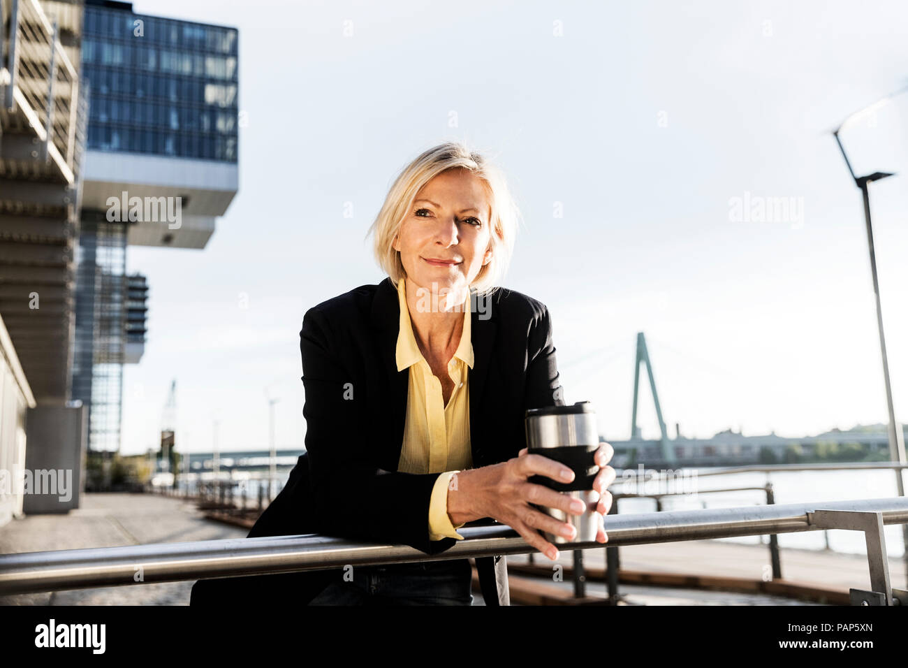 Lächelnd senior Geschäftsfrau mit Kaffee zum Mitnehmen am Flußufer Stockfoto