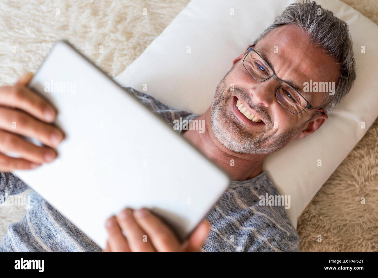 Reifer Mann lag auf Kissen mit einem Tablet Stockfoto
