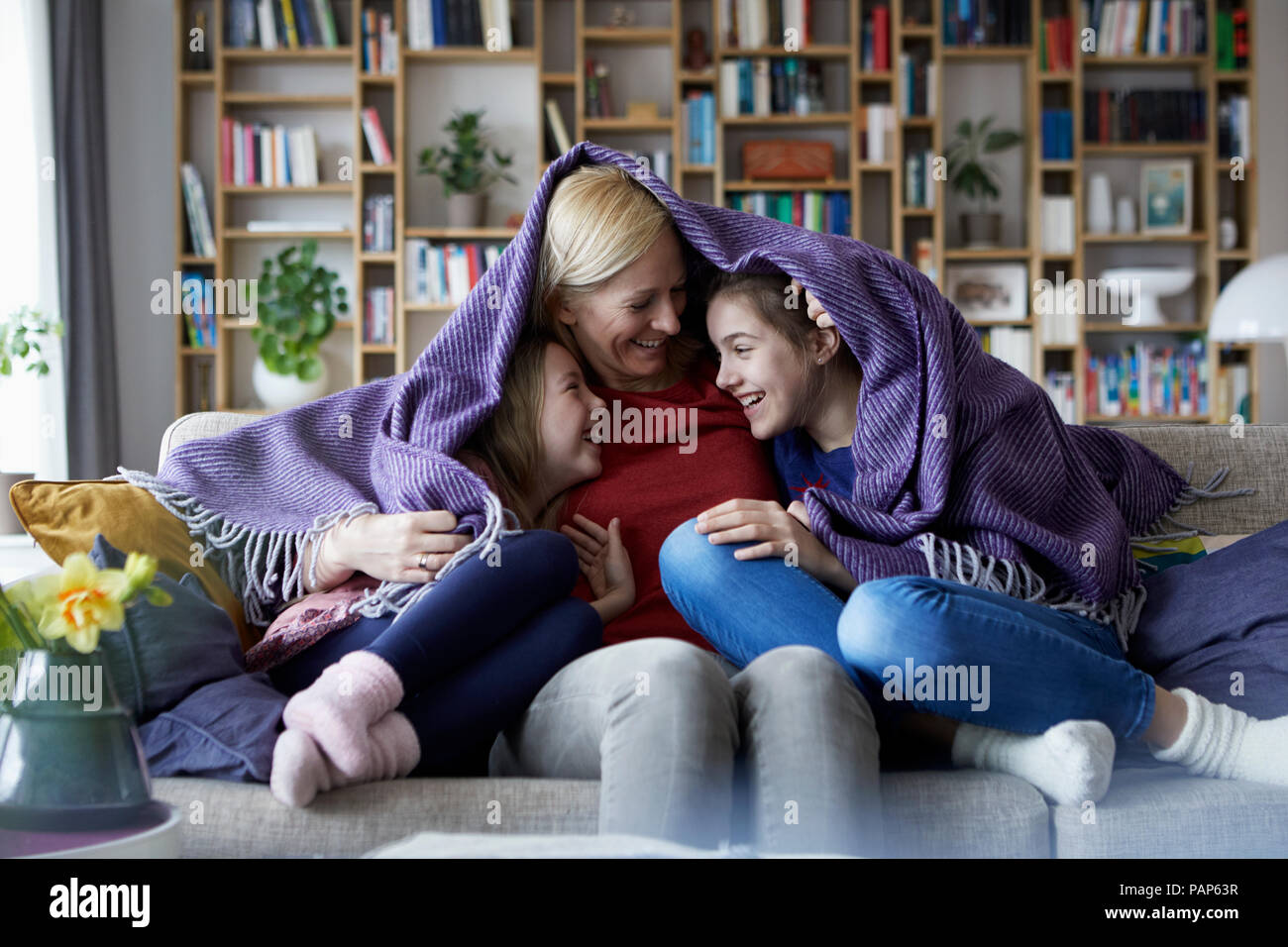 Mutter und ihre Töchter kuscheln und Spaß haben, sitzen auf der Couch, in der Decke abgedeckt Stockfoto