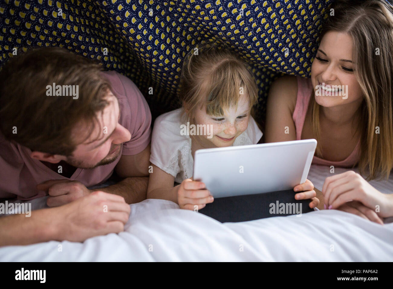 Eltern sahen etwas auf digital Tablet mit ihrer Tochter unter Decke im Bett Stockfoto