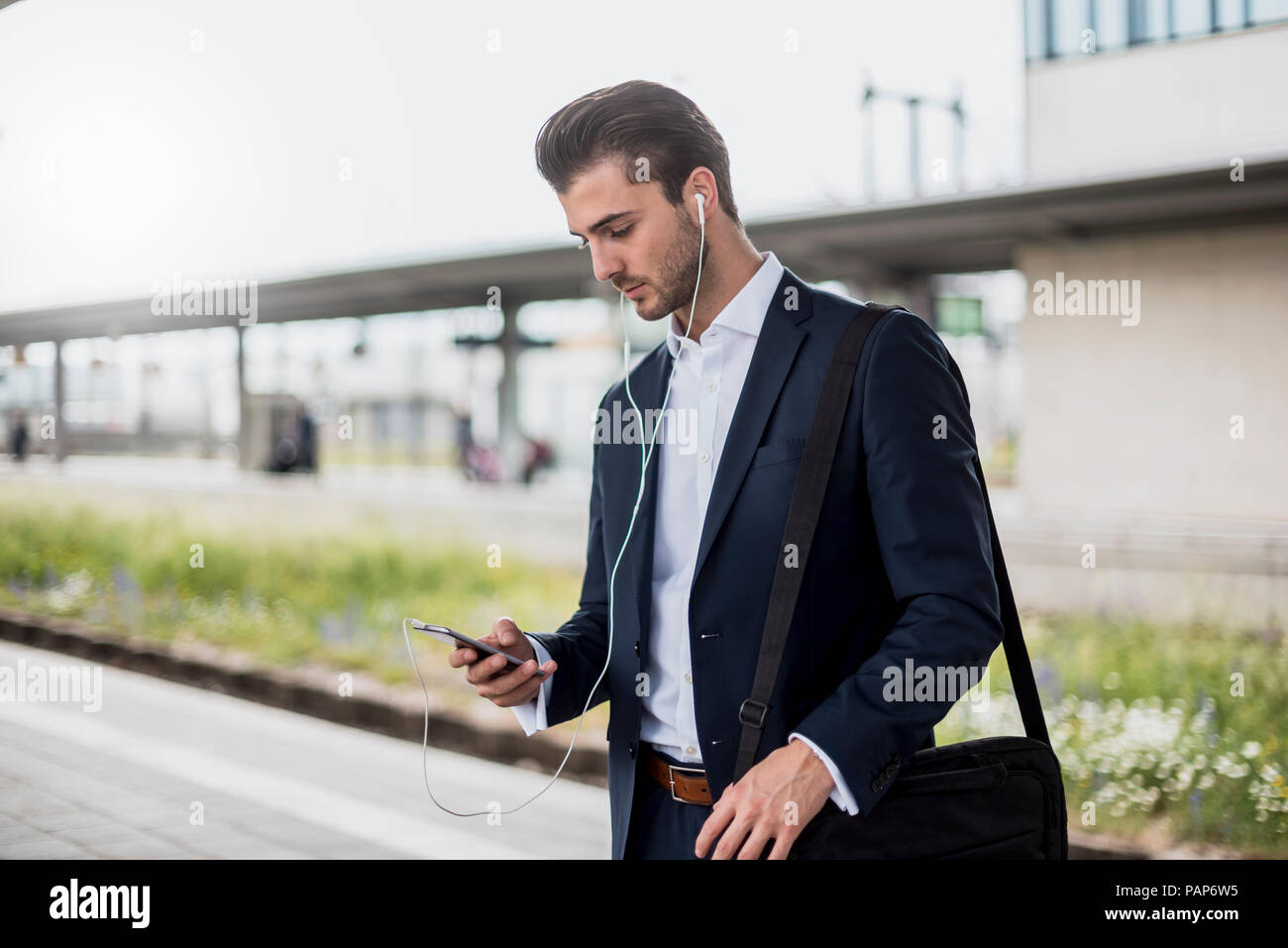 Geschäftsmann am Bahnhof mit Ohrhörern und Handy Stockfoto