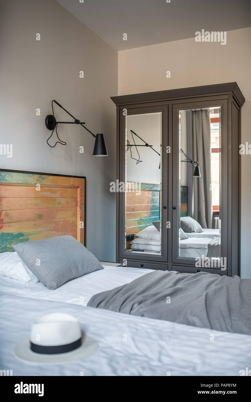 Komfortables Zimmer in einem Hotel, mit hellen Wänden. Es gibt zwei Betten mit einem bunten hölzernen bedhead, schwarz Lampen an der Wand, Fenster mit Vorhängen, Nächte Stockfoto