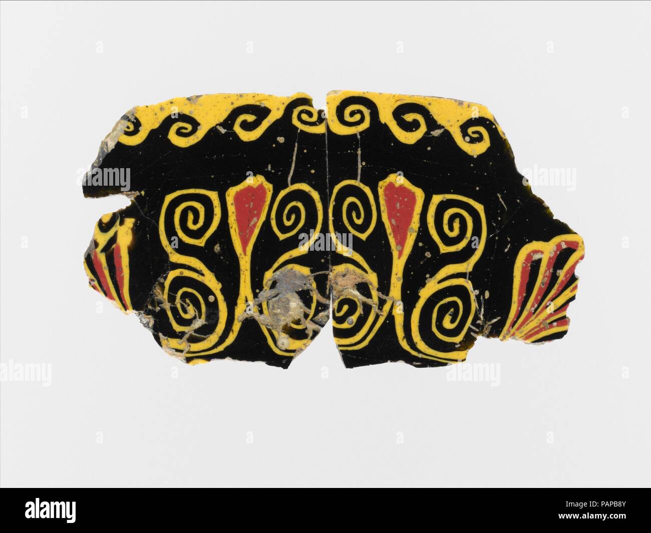 Glas Mosaik Inlay. Kultur: Ägyptische, Roman. Abmessungen: Andere: 2 1/16-in. (5.3 cm). Datum: 1. Jahrhundert v. Chr. - 1. nachchristlichen Jahrhundert. Deep Purple Masse, erscheint schwarz; Dekoration in opak Gelb und Rot. Rechteckig, dünne, flache Plakette, mit leicht abgeschrägten Kanten. Symmetrische Lotus und palmette Motiv, mit zwei langen Lotus Blumen durch doppelte Spirale Voluten und zwei palmetten an jedem Ende flankiert; oben, Continuous wave Pattern. Gebrochen und repariert mit Löchern und Rissen, und unregelmäßigen Kanten; obere Seite geschliffen und poliert; narbige Oberfläche blasen, Verwitterung an Kanten und zurück. Das Inlay ist her gemacht Stockfoto