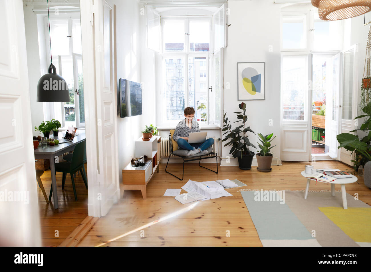 Frau sitzt im Sessel zu Hause, mit Laptop Stockfoto