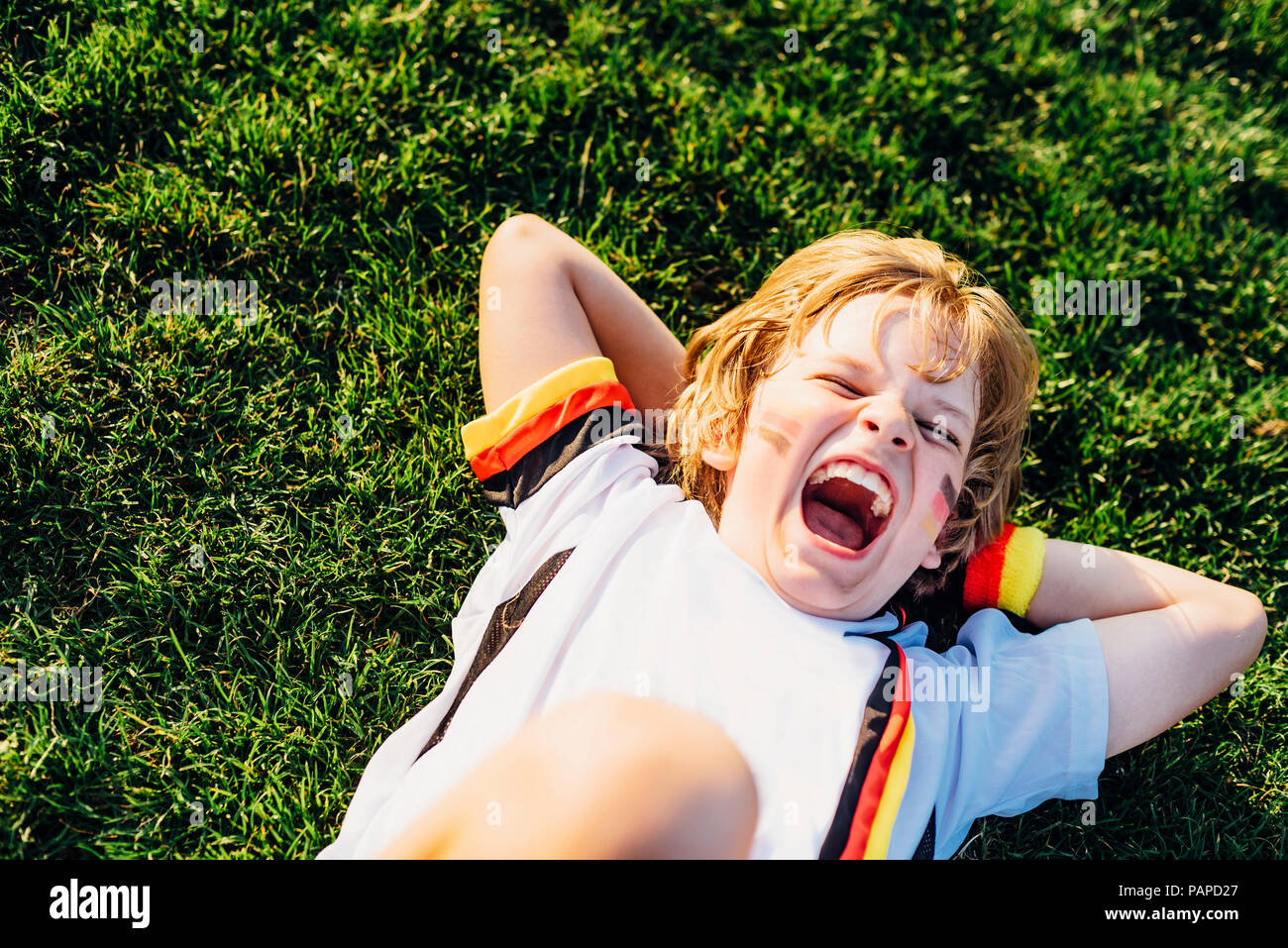 Junge im deutschen Fussball shirt liegen auf Gras, laughimg Stockfoto