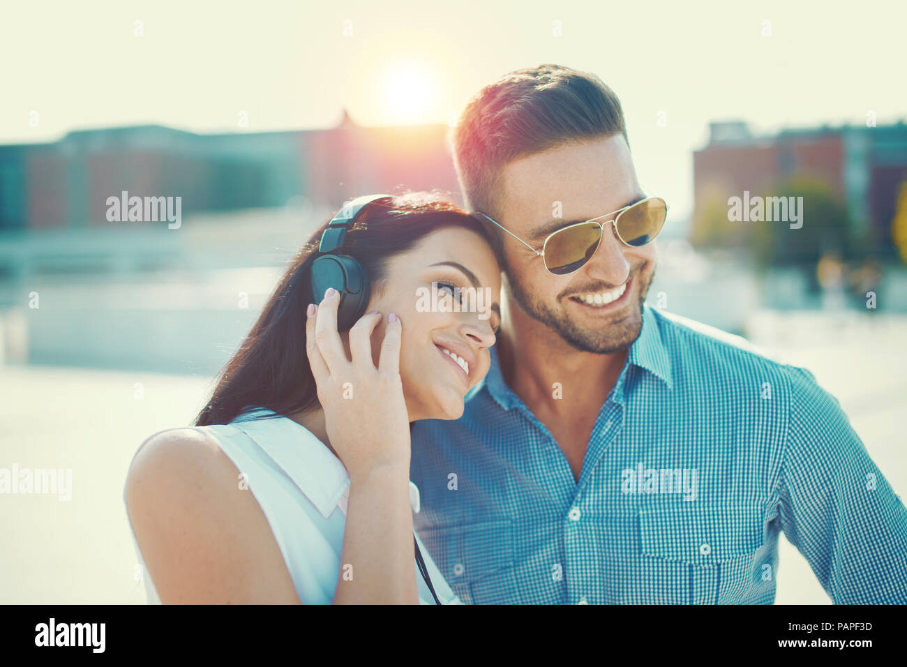 Glückliches junges Paar dating im Freien in Stadt Sonnenuntergang, Frau Musik hören über Kopfhörer Stockfoto