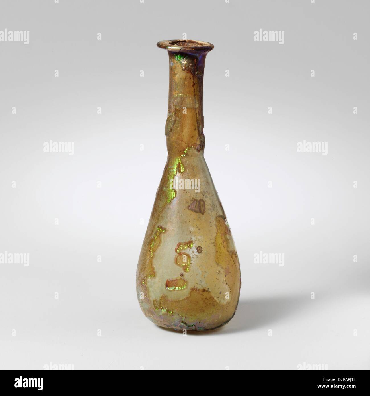 Glas Parfüm Flasche. Kultur: Roman. Abmessungen: 3 3/4 in. (9,5 cm) Durchmesser: 1 7/16 x 3/4 in. (3,7 x 1,9 cm). Datum: 1. Jh. N.CHR.. Farblos mit hellen blau-grüne Färbung. Schiefe rim ausgeklappt, über, und in, und drückte flach; schlanke, zylindrische Hals, um Base nachgerüstet; längliche piriform Körper; konkave Unterseite. Komplette, aber eine kleine Bohrung im Körper; pinprick blasen; tiefe Rillen und brillante irisierende Verwitterung. Museum: Metropolitan Museum of Art, New York, USA. Stockfoto