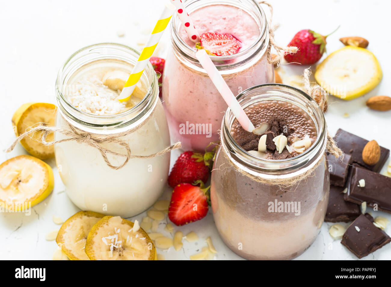 Satz von milchshake in Töpfen. Banane Schoko und Erdbeere Milchshakes mit Muttern und Kokosnuss. Sommer Nachtisch. Gesunde Ernährung auf Weiß. Stockfoto