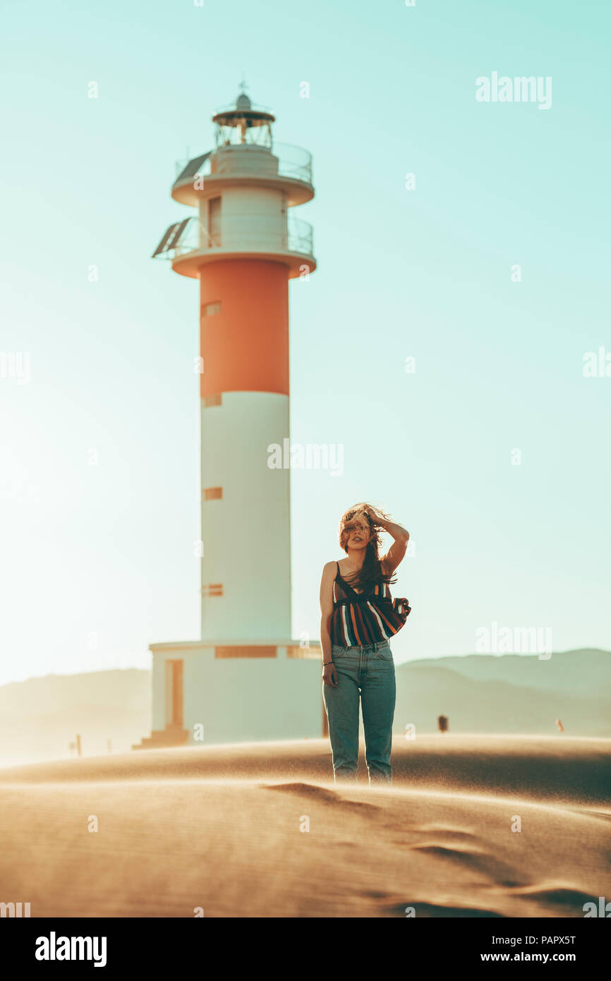 Junge Frau mit windswept Haare stehen in der Wüste Landschaft am Leuchtturm Stockfoto