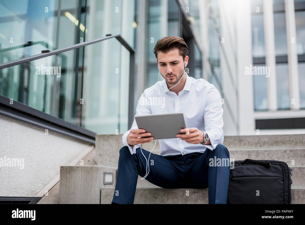 Unternehmer sitzen auf Treppen mit Ohrhörern und Tablet Stockfoto