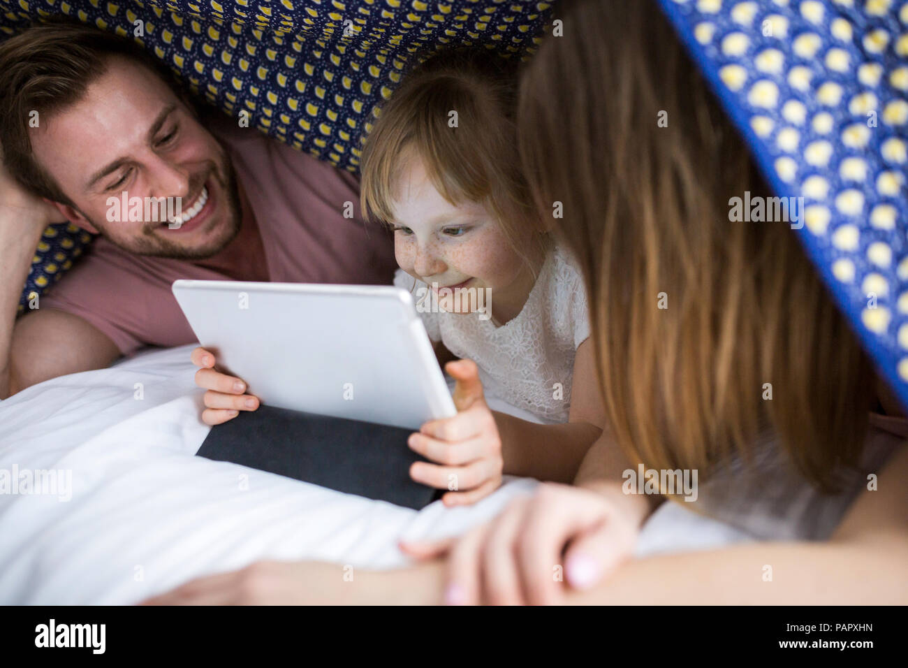 Eltern sahen etwas auf digital Tablet mit ihrer Tochter unter Decke im Bett Stockfoto
