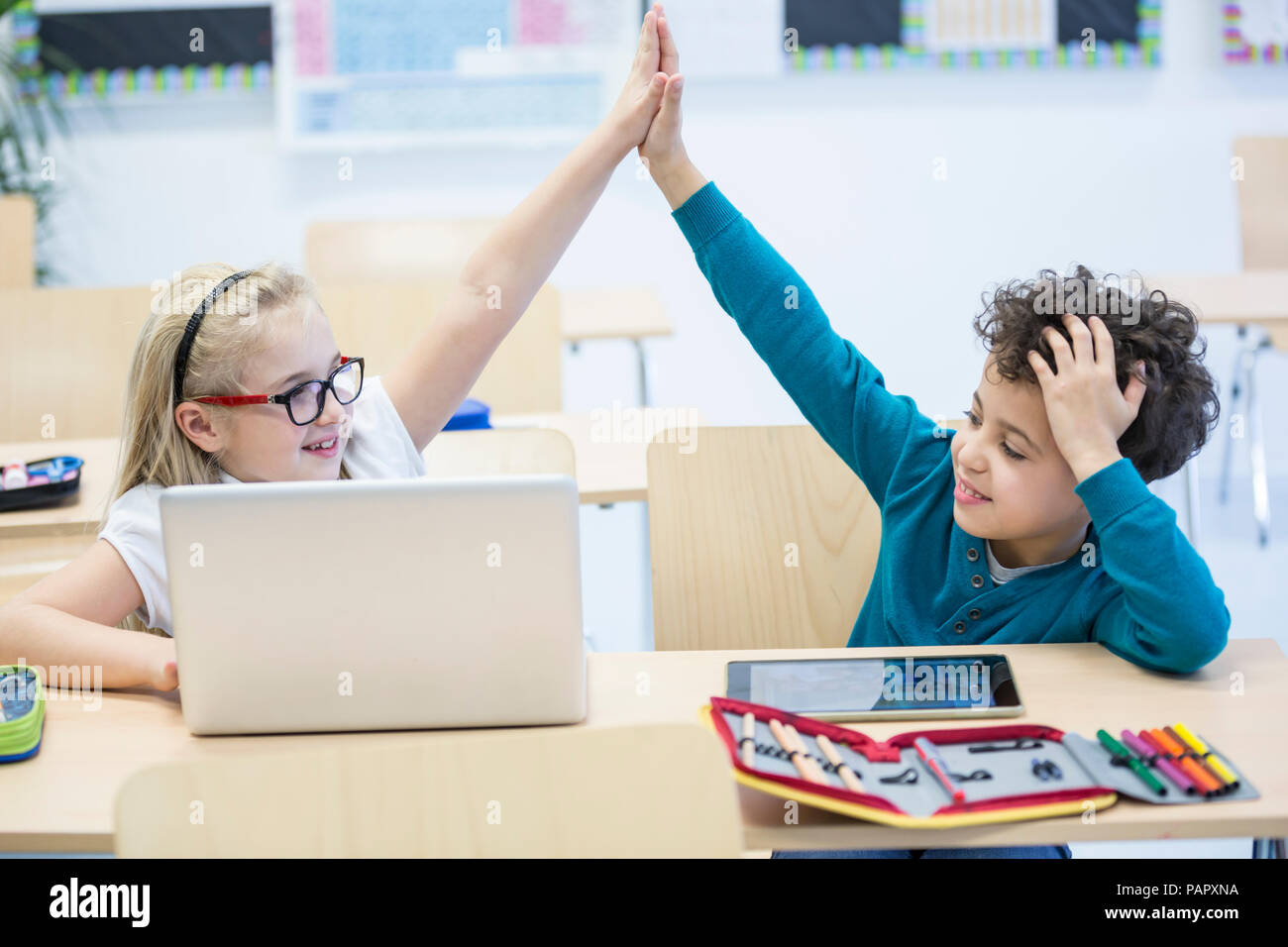 Schüler und Schülerin mit Laptop high fiving in der Klasse Stockfoto